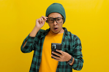 Shocked Asian man, sporting a beanie hat and casual shirt, adjusts his glasses while gazing at his...