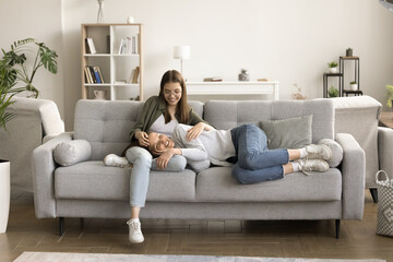 Happy mom and teen daughter resting on comfortable couch in modern home interior. Positive relaxed...