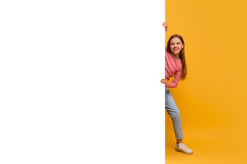 A young girl wearing a pink shirt is leaning casually against a vibrant yellow wall. Her posture is...