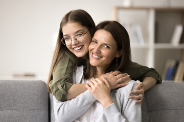 Happy lovely teenage girl in glasses hugging beautiful mom from behind with love, trust, gratitude,...