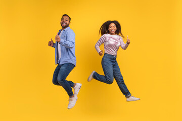 African American man and woman are captured mid-air as they jump energetically, displaying a moment of joy and freedom, yellow background - Powered by Adobe