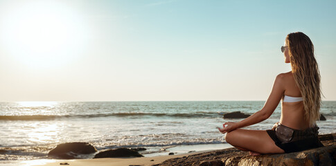 A serene woman in meditation pose on the tropical sea beach at sunset. A young adult female doing...
