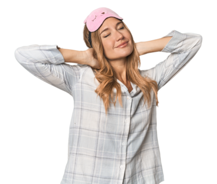 Blonde in pajamas with sleep mask stretching arms, relaxed position.