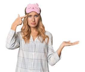 Blonde in pajamas with sleep mask holding and showing a product on hand.