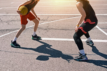 Fototapeta premium Two teenage girls play street basketball on a court in the city.