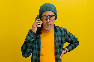 Annoyed Asian man, dressed in beanie hat and casual clothes, engages in a phone conversation,...