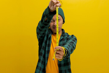 An Asian man, dressed in a beanie hat and casual clothes, measures his height using a yellow...