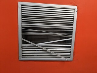Damaged metal ventilation grille on a vibrant orange wall