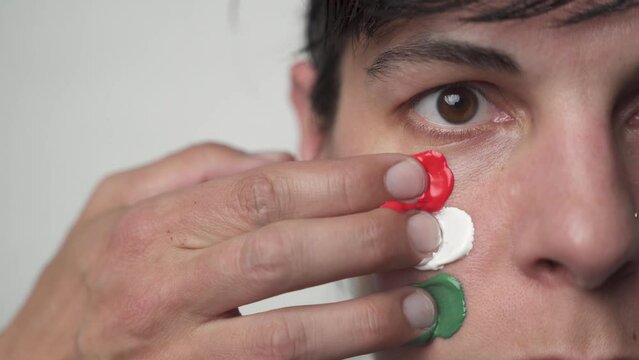 Supporter painting face and looking at camera. Sport fan woman preparing for the game. Colored face with flag colors red, white and green. 