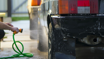 water from a hose from a spray bottle washes the car. Car washes use high pressure water sprays, detergents. washes the car at home in the garage. black car rear view