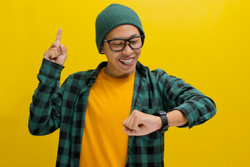 Enthusiastic Asian man in a beanie wearing eyeglasses, points upwards impatiently. He checks his...