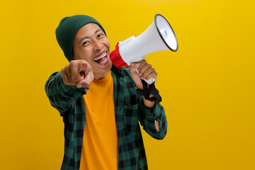Excited Asian man in a beanie hat and casual shirt shouts into a megaphone, pointing at the camera,...
