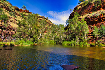 Red rocks huge boulder and green trees reflecting in the clear water of a pool in the Kalamina Gorge, Karijini National Park, Western Australia
 - Powered by Adobe