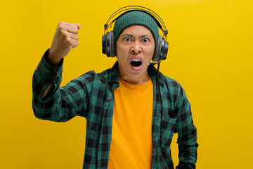 Furious Asian man in a beanie and casual clothes, clenches his fist while listening to music or...