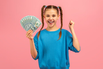 A young girl is seen holding a fan of money in her hand. She looks curious and excited as she grips...