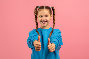 A young girl child with two neatly braided hair strands is smiling and showing a thumbs up gesture, indicating positivity and approval.