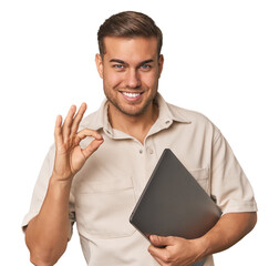 Man holding laptop, studio cheerful and confident showing ok gesture.
