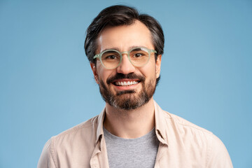 Happy young man in glasses posing in studio, looking at camera. Isolated on blue background