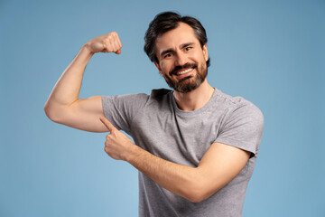 Smiling happy healthy man showing his muscles, flexing biceps on arm, isolated on blue