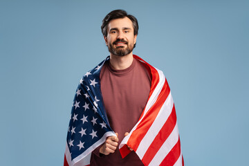 Portrait of young bearded man holding a USA american flag isolated over blue background