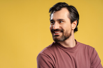 Fototapeta premium Happy bearded young man posing in studio looking to the side. Isolated on yellow