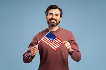 Happy young man showing national flag of United States, posing in studio, isolated on blue