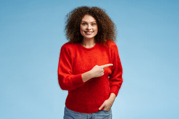 Excited, smiling woman with curly hair pointing with finger on copy space, looking at camera