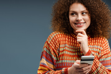 Smiling young woman with curly hair holding mobile phone, looking away