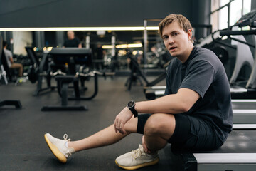 Portrait of exhausted runner taking break at gym sit on treadmill. Portrait of exhausted sweaty male hard breathing after cardio exercise running workout. Weary man sit on fitness treadmill relax.