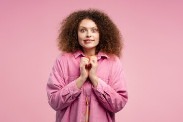 Excited woman with curly hair, hipster looking at camera standing isolated on pink background