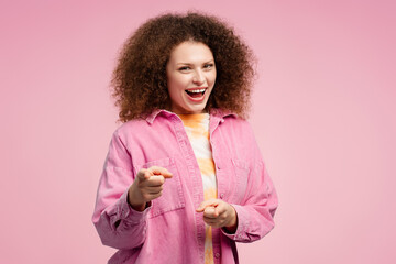 Excited, smiling woman with curly hair wearing casual clothes pointing fingers, looking at camera