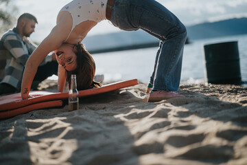 A young woman practices yoga on a surfboard at a sandy lake beach with a friend nearby, depicting...