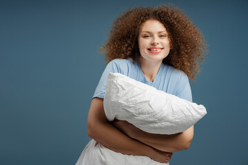 Cheerful beautiful woman with curly hair holding pillow, smiling, looking at camera