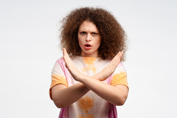 Serious, angry, young woman with curly hair showing with hands no gesture, stop sign, arms crossed