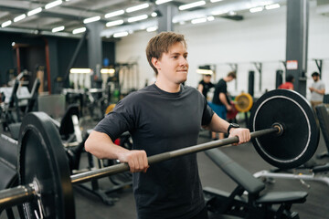 Medium shot of sportsman hard time performing barbell shoulder press in gym. Athletic male holding barbell on front of shoulders and presses barbell overhead. Concept of healthy sports life.