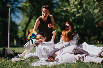 Four friends relax and play on a sunny day in the park, one playfully pointing with a colorful...