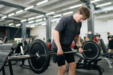 Medium shot of motivated beginner sportsman in casual sport workout outfit hard time performing exercises. lifting barbell training exercising deadlift at gym. Concept of healthy lifestyle.