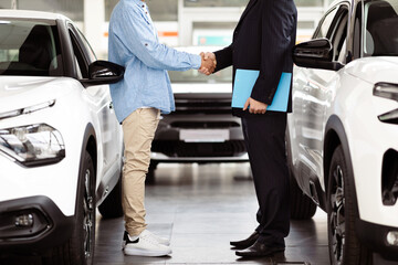 Cropped of two men are standing inside a bright and spacious car showroom. They are shaking hands...