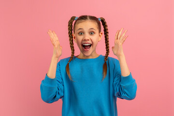 A young girl wearing a bright blue sweater stands against a vibrant pink backdrop, her hands raised...