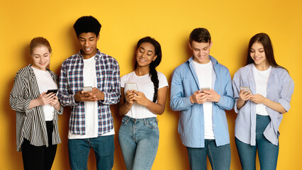 A diverse group of five multiethnic teenagers stand side-by-side against a vibrant yellow backdrop,...