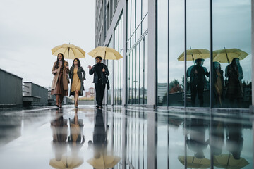 Group of friends walking with umbrellas reflecting on wet city sidewalk.