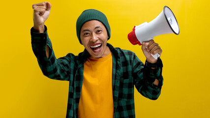Happy and successful Asian man in a beanie hat clenches his fist in a victory gesture while...