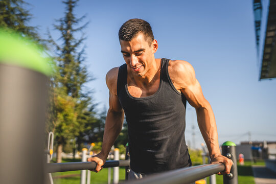 One man muscular male athlete training dips outdoor in sunny day