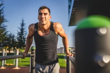 One man muscular male athlete training dips outdoor in sunny day