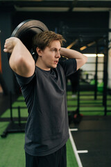 Vertical portrait of motivated beginner sportsman holding and rotating weight disc plate overhead during sport workout training in modern gym. Concept of healthy lifestyle, physical sport activity.