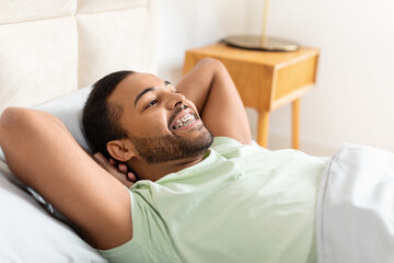African American man is laying in bed with his head resting on the pillow. He appears relaxed and...