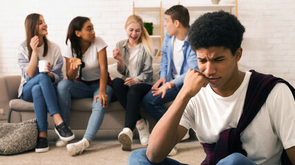 Black teenage boy appears visibly stressed and uncomfortable in the foreground while a group of his...