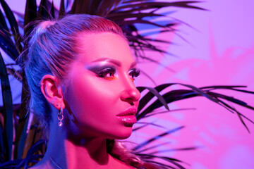 Fashion model woman with a bright make-up in colourful bright neon uv lights posing in studio.