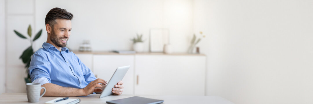 Handsome Young Businessman Using Digital Tablet At Workplace In Office, Browsing New Application Or Social Media, Free Space