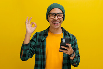 An Asian man, donning a beanie hat, casual shirt, and eyeglasses, flashes an OK sign towards the...